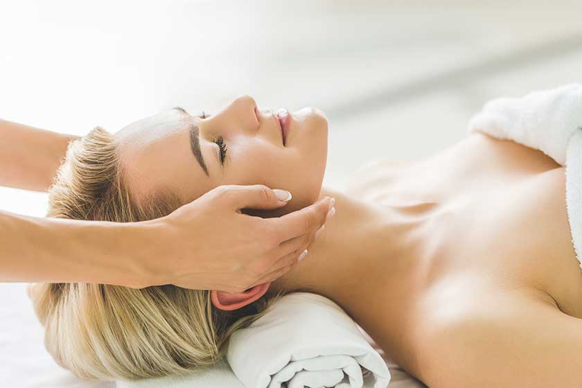 Smiling young woman having facial massage at salon